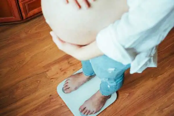 Image of woman weighing herself and experiencing weight gain through pregnancy Wigan